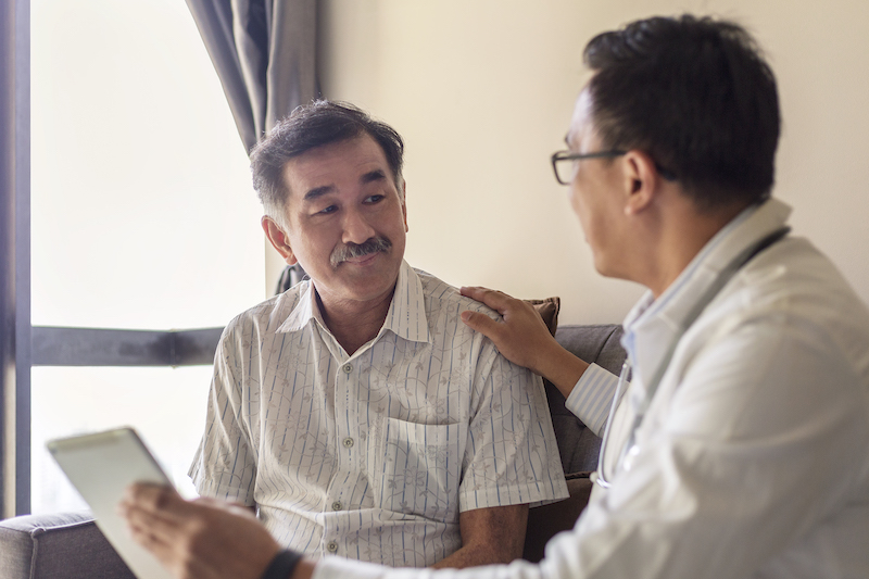 doctor showing mid-aged asian man a chart. doctor's hand on the mans's shoulder 
